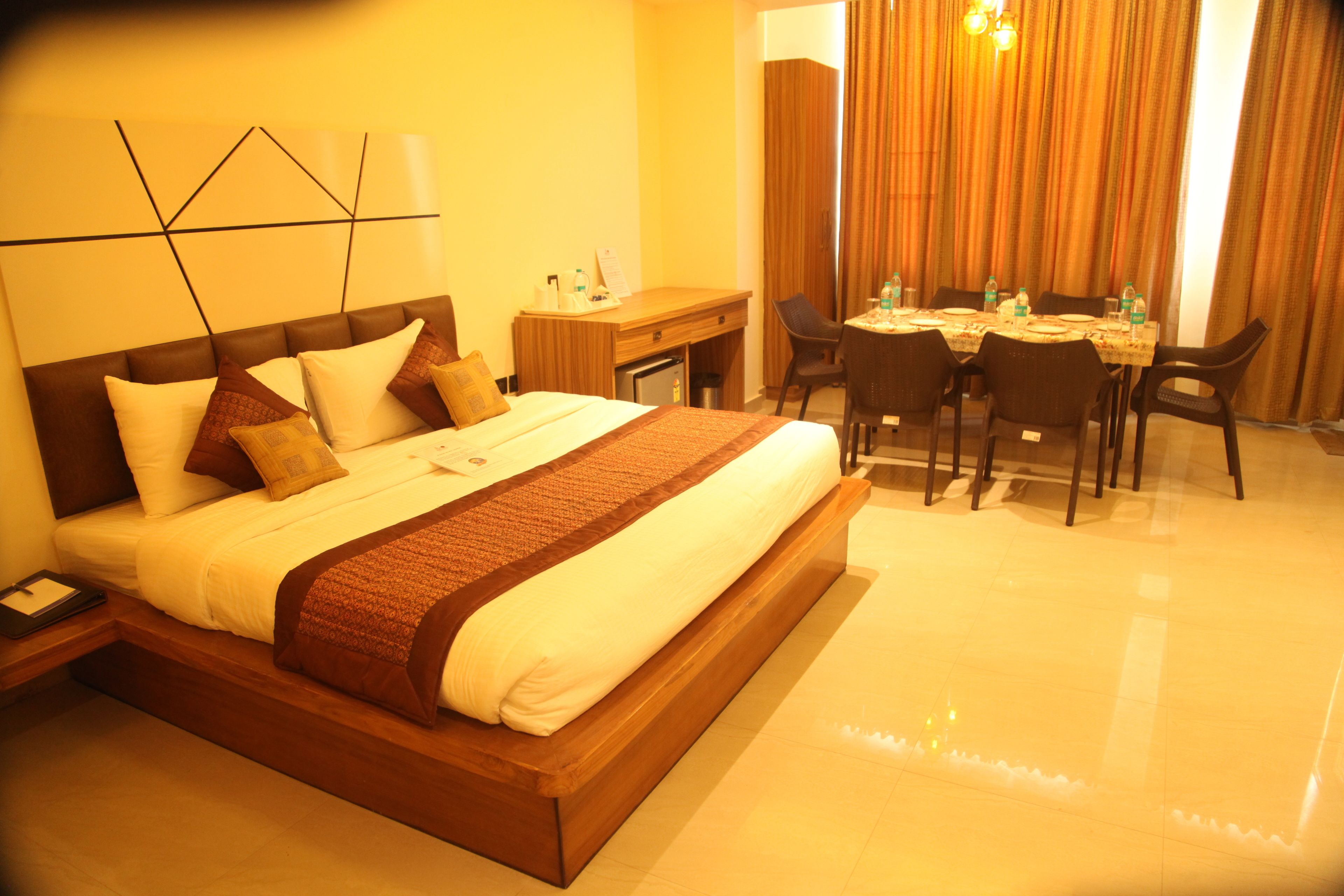 A hotel room with a large bed, a desk, and a dining table with chairs.