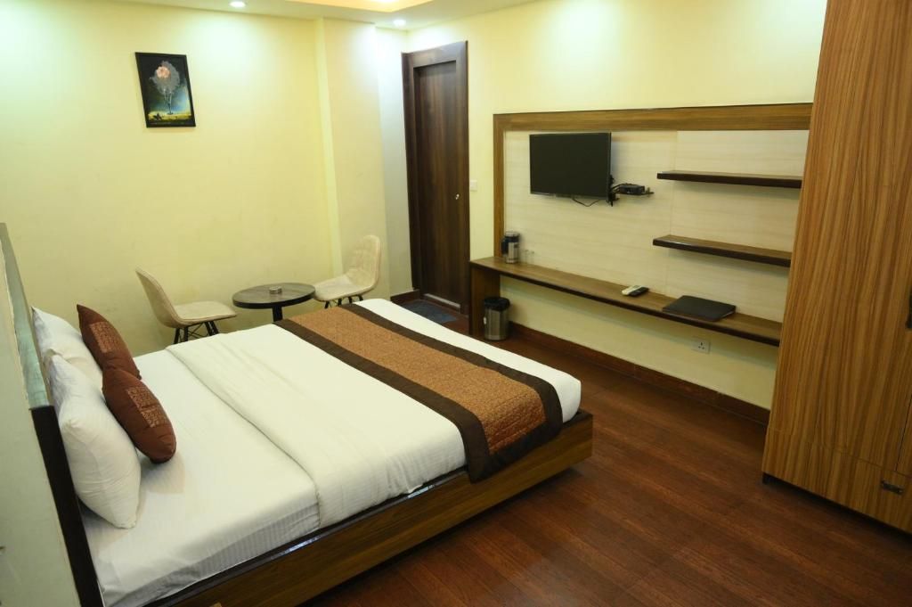 A hotel room with a bed, a desk, a chair, a television, and a shelf.