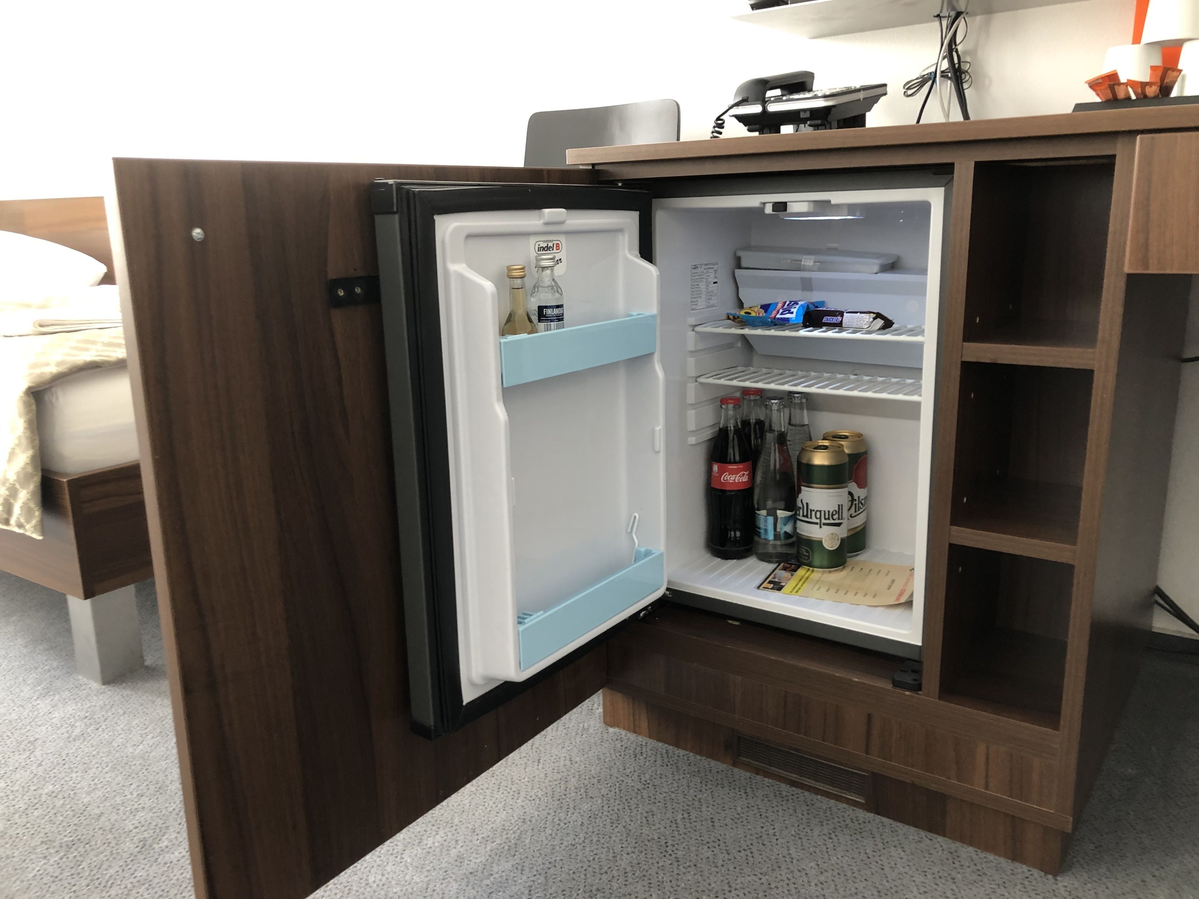 A compact refrigerator with a freezer compartment, containing beverages and a bottle of Fanta.