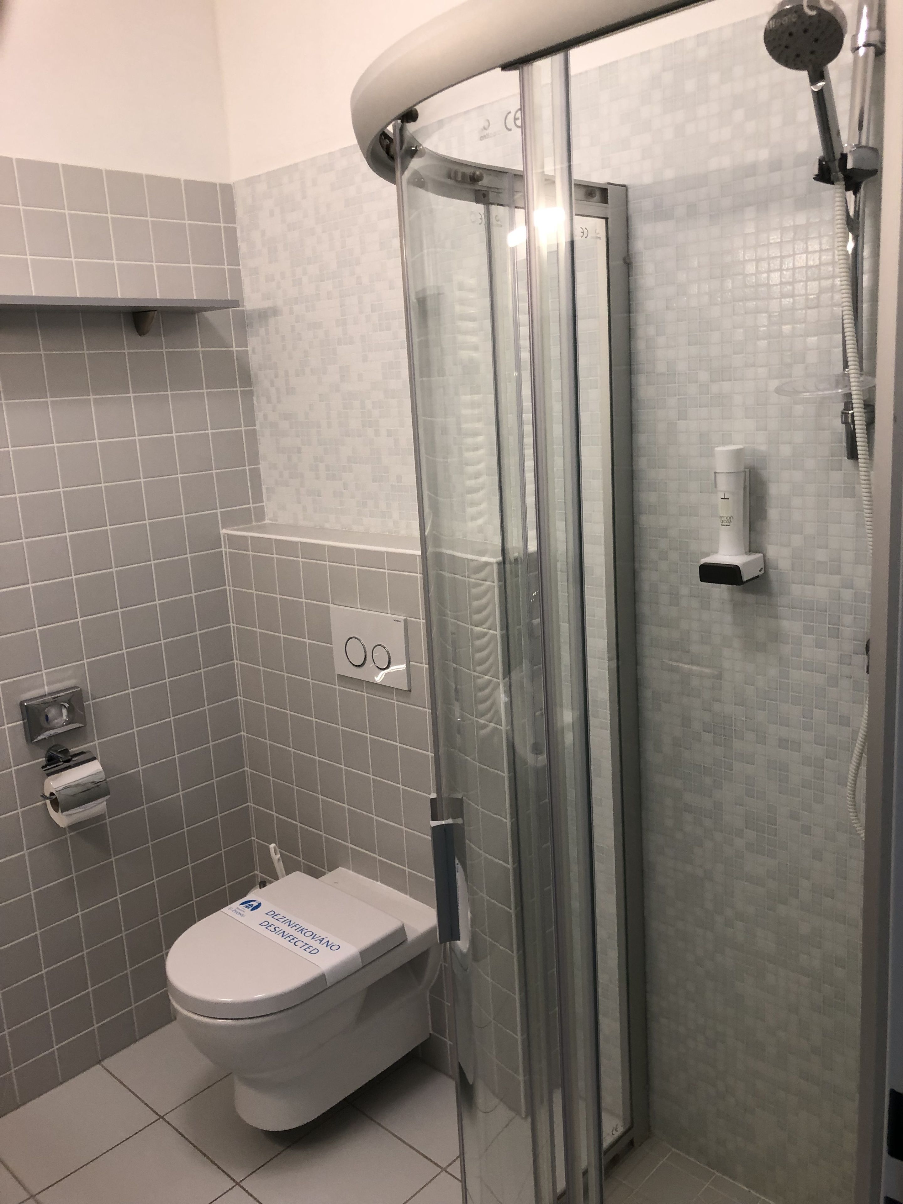 A bathroom with a toilet, a glass shower enclosure, and a hand dryer.