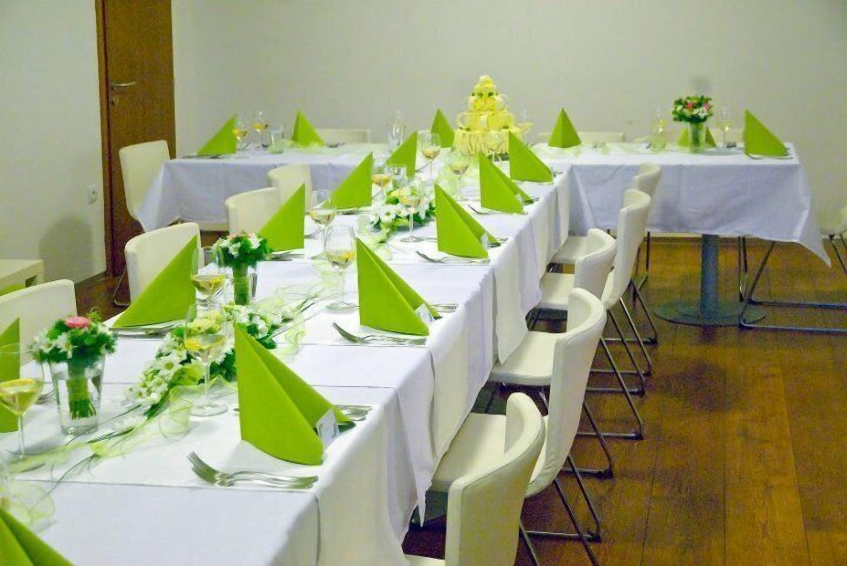 A banquet hall with long tables set for a formal event, each with white tablecloths, green centerpieces, and white chairs.