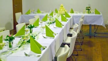 A banquet hall with long tables set for a formal event, each with white tablecloths, green centerpieces, and white chairs.
