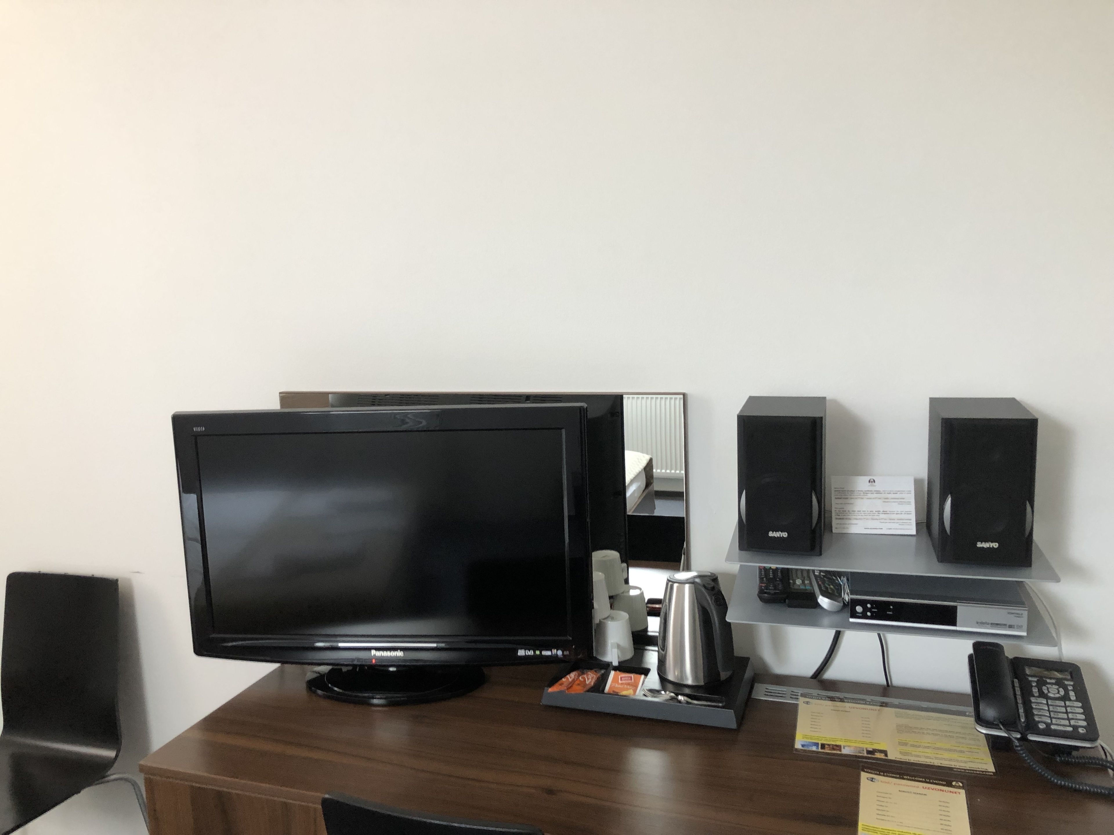 Ein Hotelzimmer mit einem großen Flachbildfernseher, einer Kaffeemaschine, einem Telefon und einem kleinen Schreibtisch mit Tastatur und Monitor.