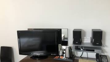 Ein Hotelzimmer mit einem großen Flachbildfernseher, einer Kaffeemaschine, einem Telefon und einem kleinen Schreibtisch mit Tastatur und Monitor.