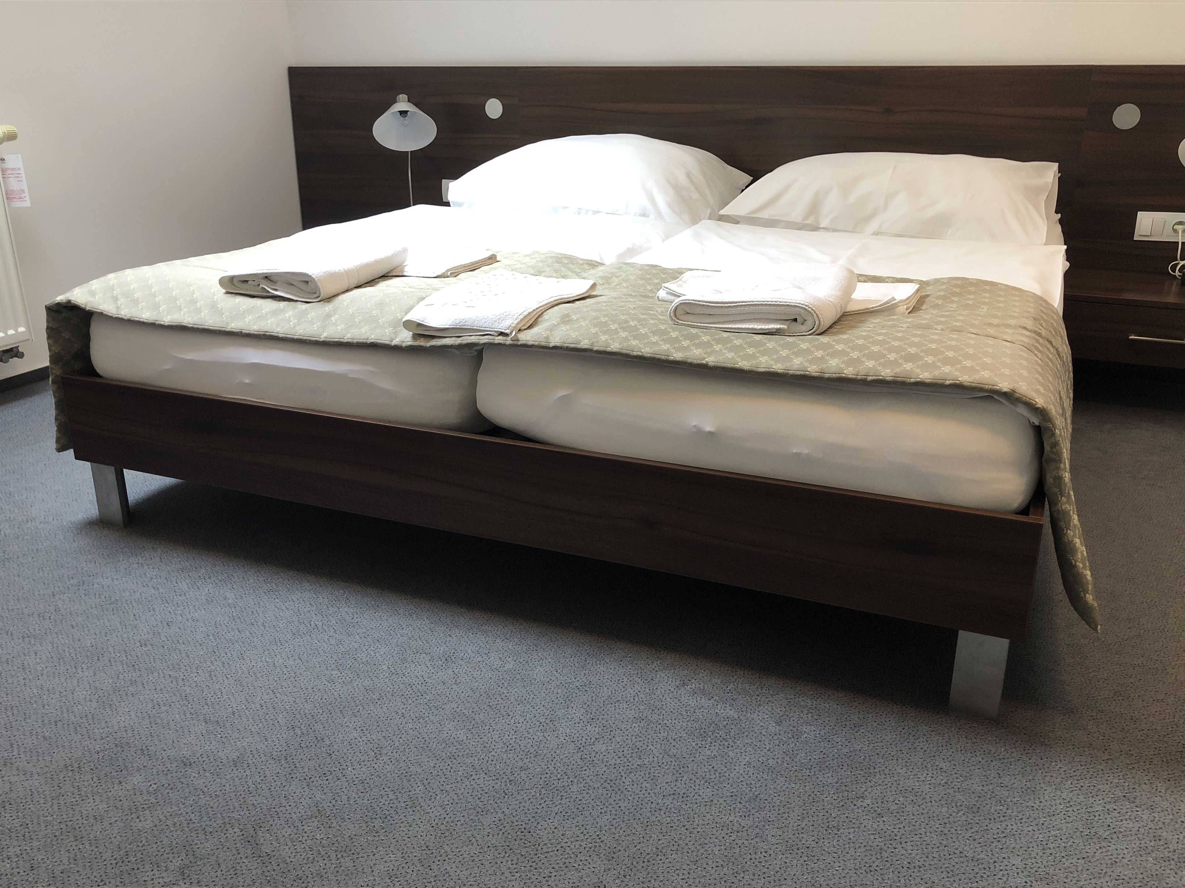 Een net opgemaakt bed met een houten hoofdbord, witte lakens en een groene, gestreepte deken.