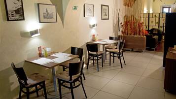A dining area with tables and chairs, framed pictures on the walls, and a decorative plant.