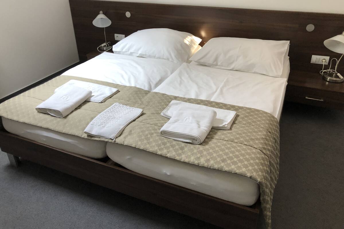 Una cama bien hecha con sábanas blancas, una colcha estampada y dos lámparas de noche.