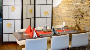 Comedor con una mesa de madera preparada para cuatro personas, sillas blancas y una pared de piedra al fondo.
