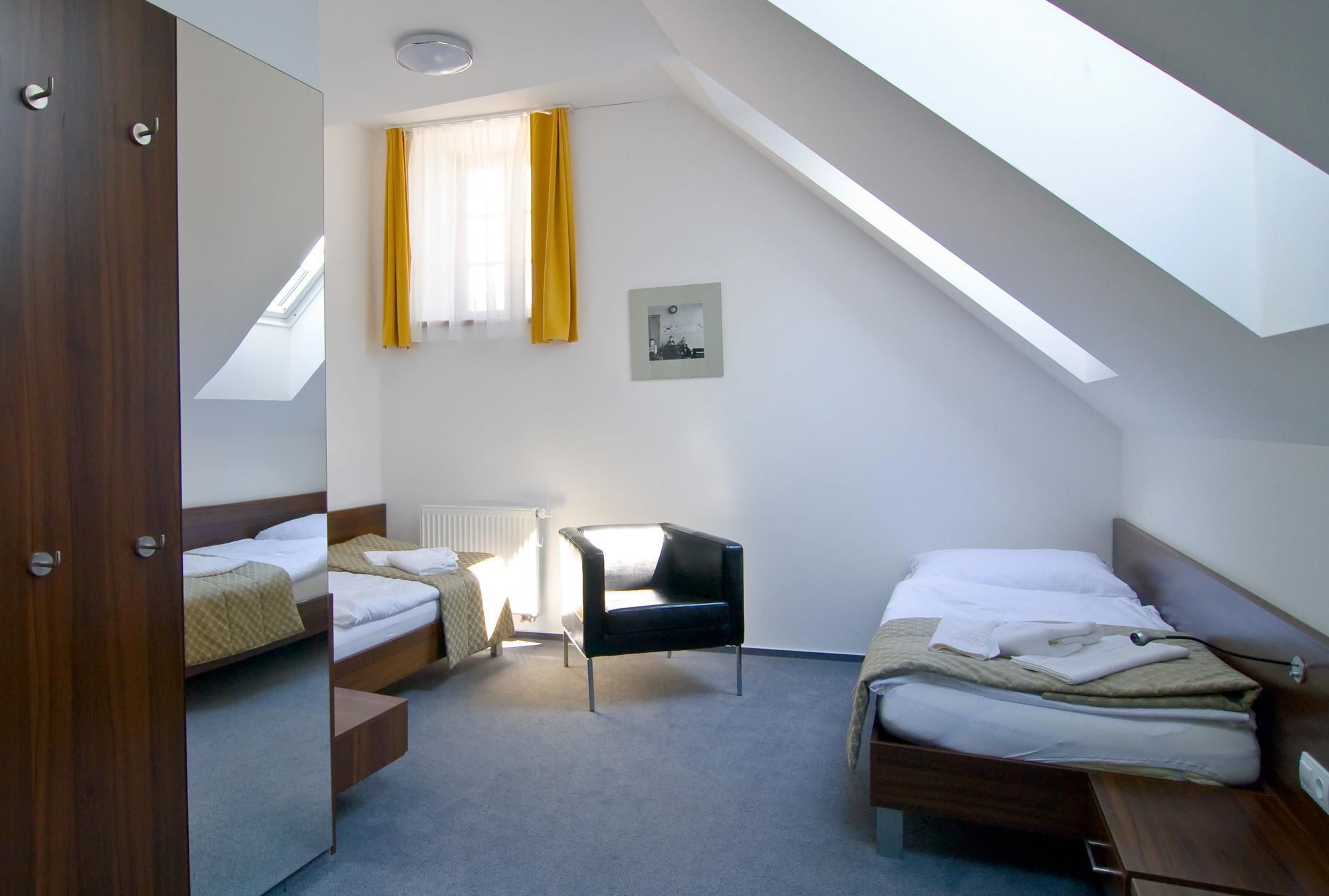 Ein Zimmer mit schrägem Dach, zwei Betten, einem Sessel und einer Heizung.