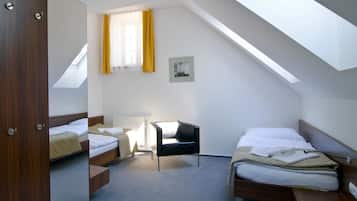 Ein Zimmer mit schrägem Dach, zwei Betten, einem Sessel und einer Heizung.