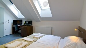 Una habitación de hotel con una cama, un escritorio, un televisor y un tragaluz.
