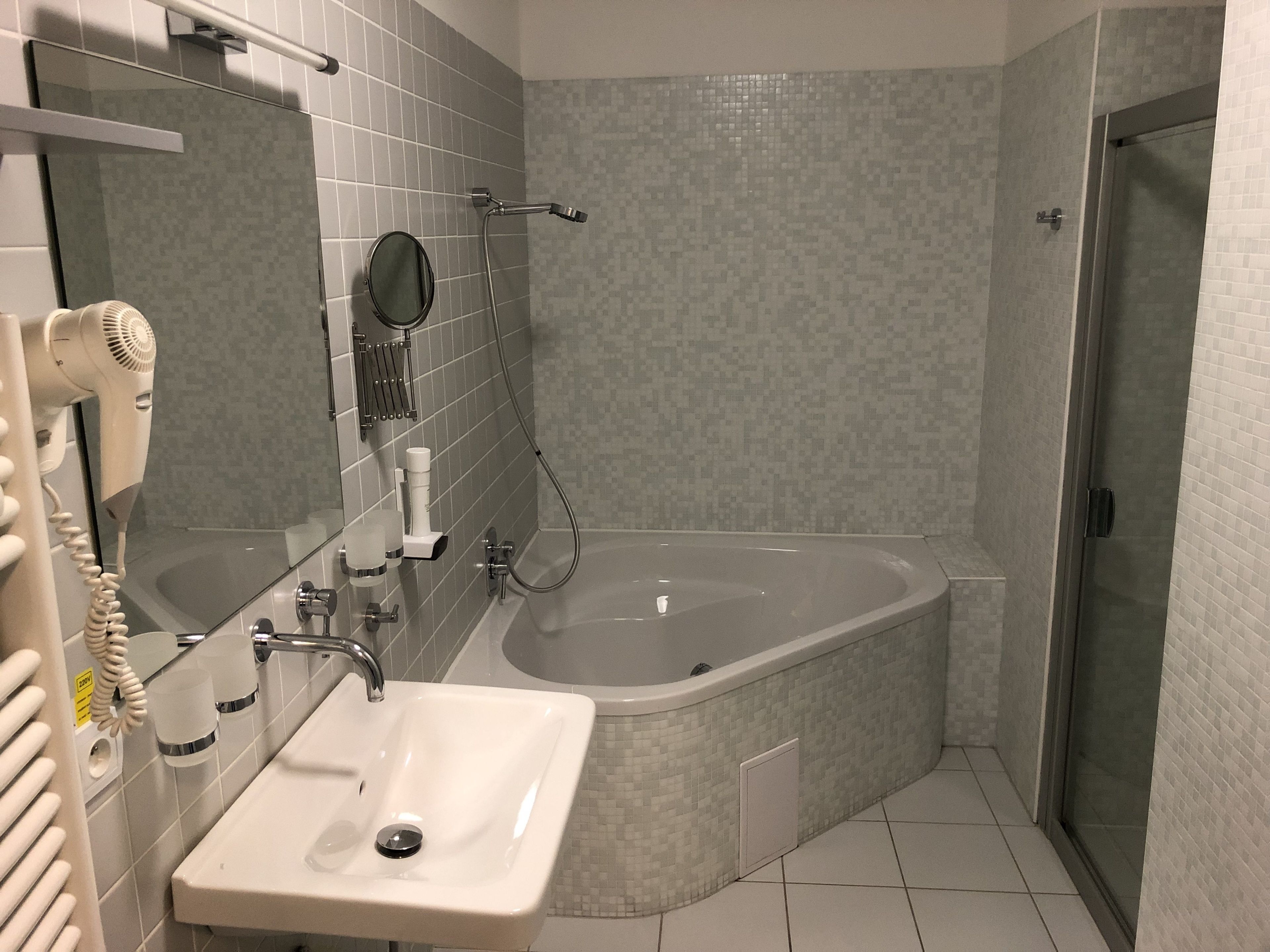 A bathroom with a sink, mirror, hairdryer, and shower.