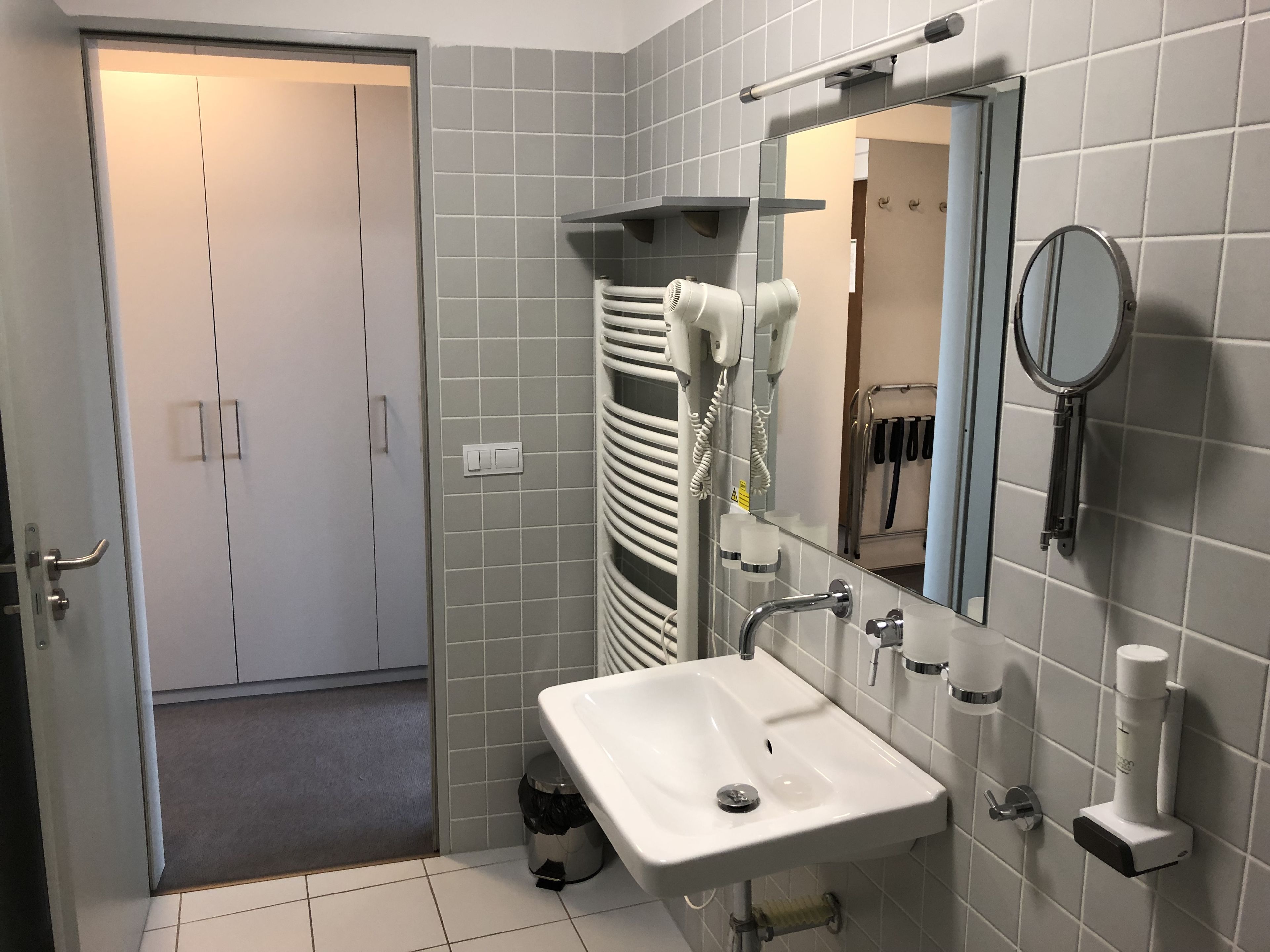 A bathroom with a white sink, mirror, towel rack, and a trash bin.
