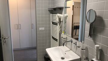 A bathroom with a white sink, mirror, towel rack, and a trash bin.
