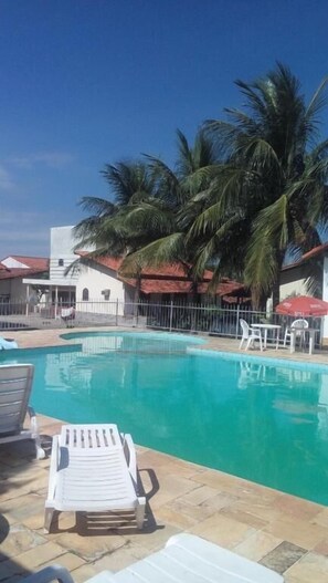 A swimming pool with lounge chairs, palm trees, and a building with a red roof in the background.