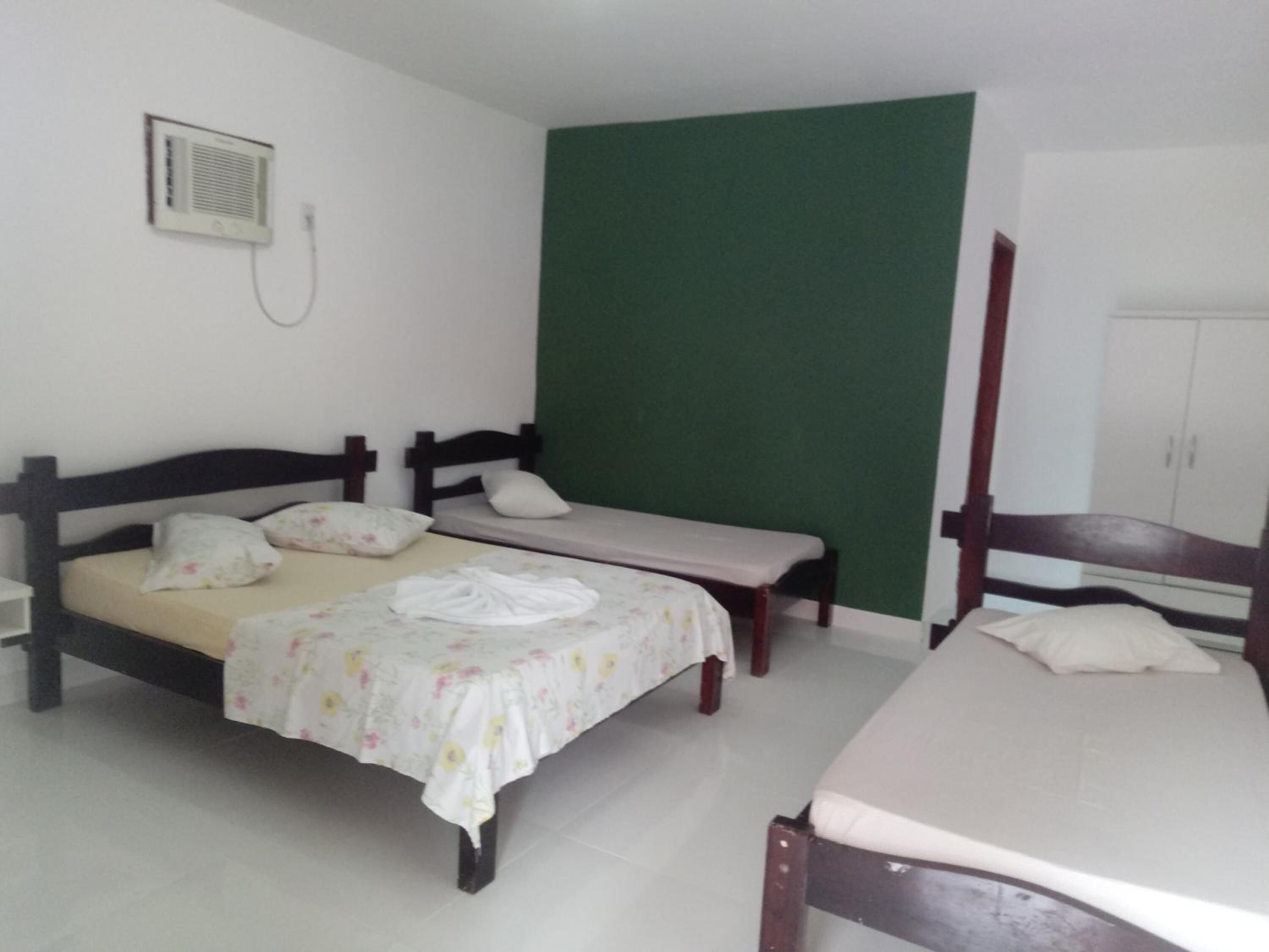 Quarto com duas camas, parede verde, armário branco e aquecedor fixado na parede.