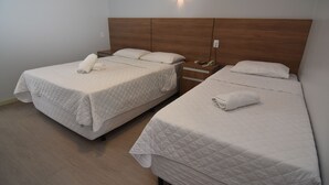 Dos camas individuales con cabeceras de madera, una mesita de noche con lámpara y un aplique de pared.