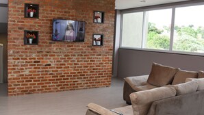 Una sala de estar con pared de ladrillo, un televisor de pantalla plana y un ventanal grande.