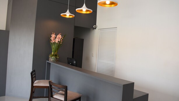 Un área de recepción moderna con una pared oscura, un mostrador de recepción, una silla y tres lámparas colgantes.