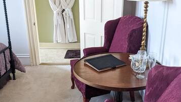 A room with a round wooden table, two purple armchairs, a white door, and a robe hanging on a hook.