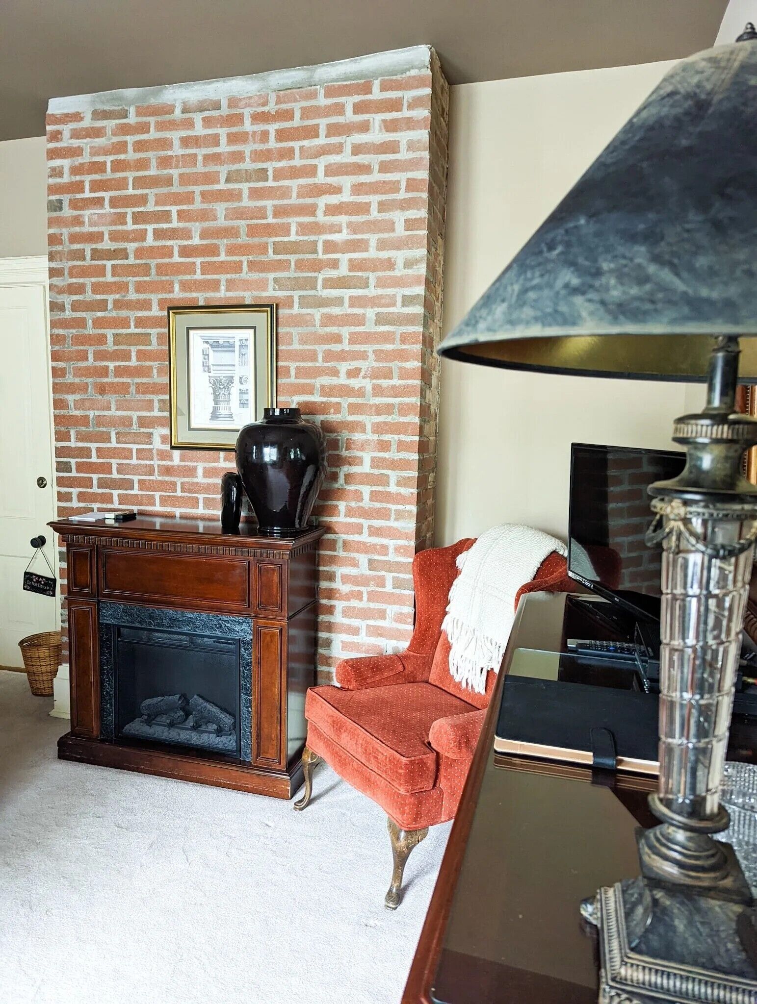 Una sala de estar con pared de ladrillo, chimenea, un sillón rojo y una lámpara de mesa.