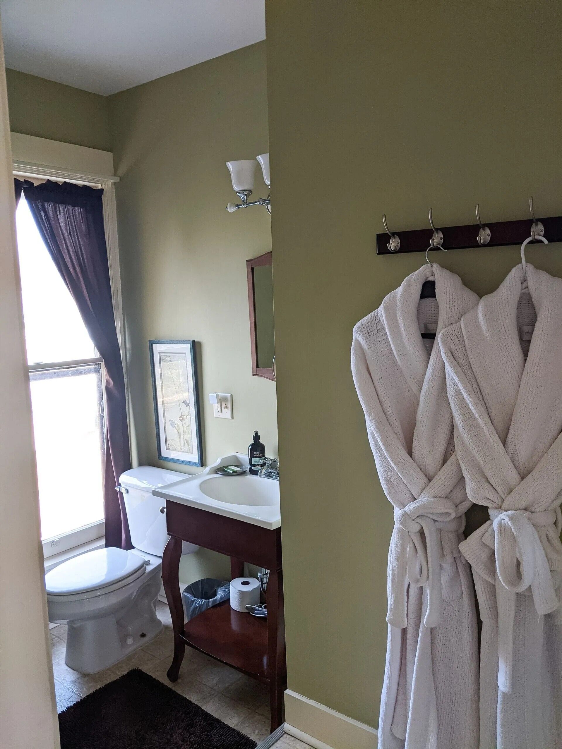 A bathroom with a toilet, sink, and a robe hanging on a rack.