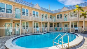 A pool area with a circular pool, a balcony with white railings, and a building with multiple windows and doors. - 🌴 Tranquil Coastal Escape @ Clearwater Beach Suites | Steps to Sand • Heated Pool ➠ CBS 203 (Clearwater)