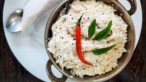 Una ciotola di riso con peperoncino rosso e foglie verdi su un piatto bianco, con un cucchiaio.