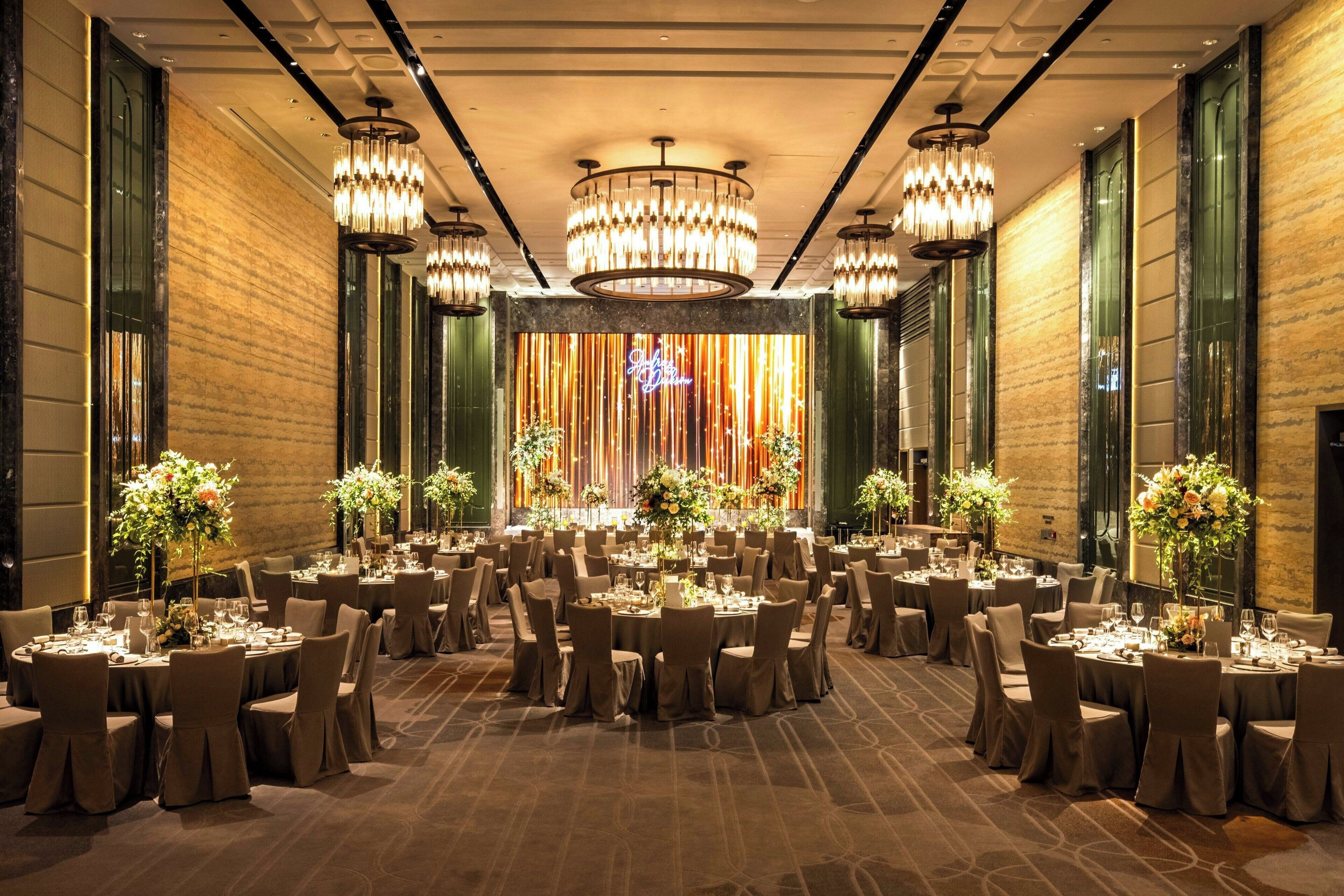 A banquet hall with round tables, chairs, and chandeliers.