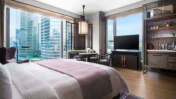 A modern hotel room with a large bed, a dining area, a TV, and a view of the cityscape.