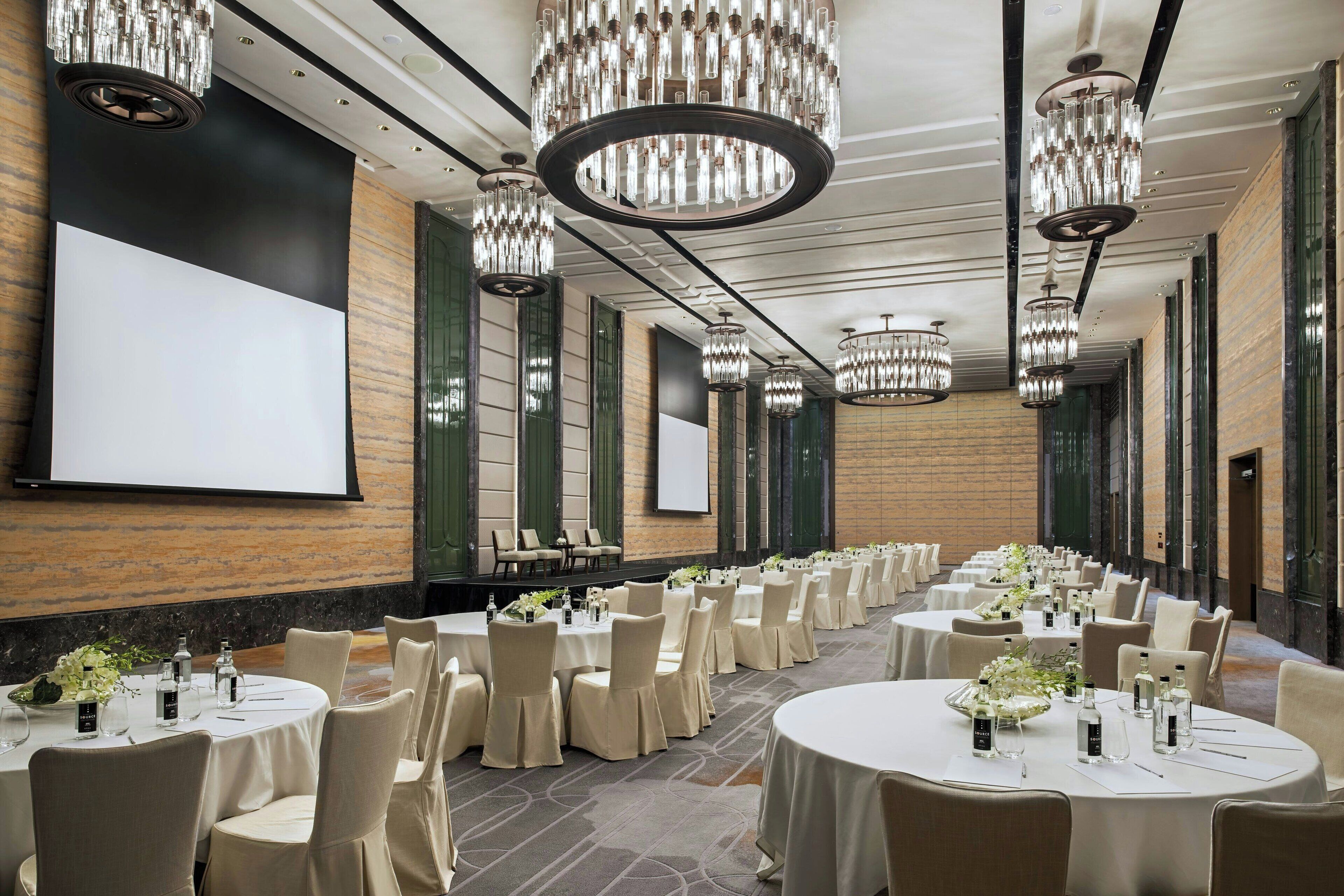 A conference room with round tables, chairs, and chandeliers.