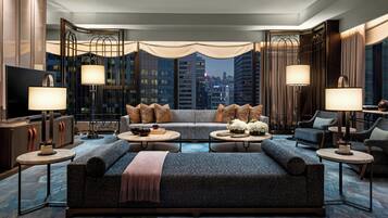 A modern living room with a large sofa, two side tables, a television, and a city view through large windows.
