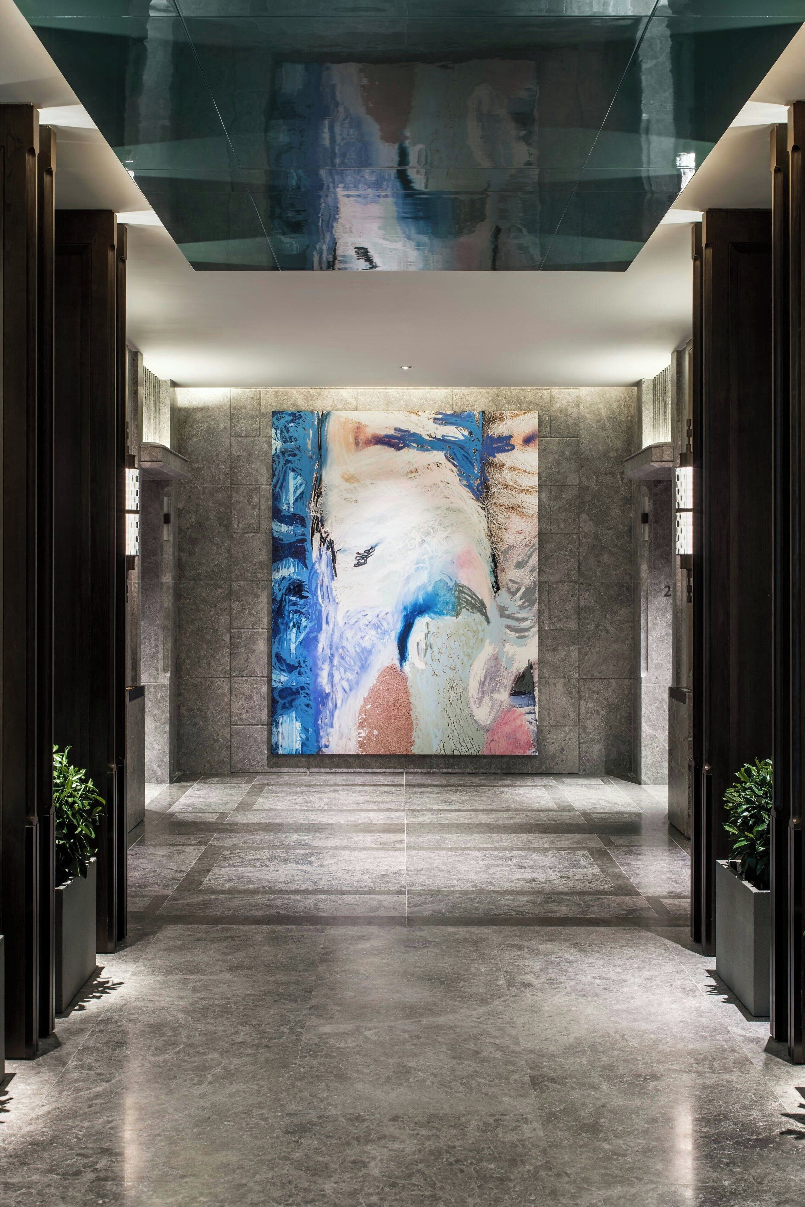 Um lobby moderno com uma grande pintura abstrata, piso de mármore e paredes em tons escuros.
