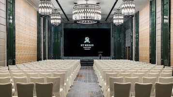 A conference room with rows of white chairs, a large screen at the front, and chandeliers.
