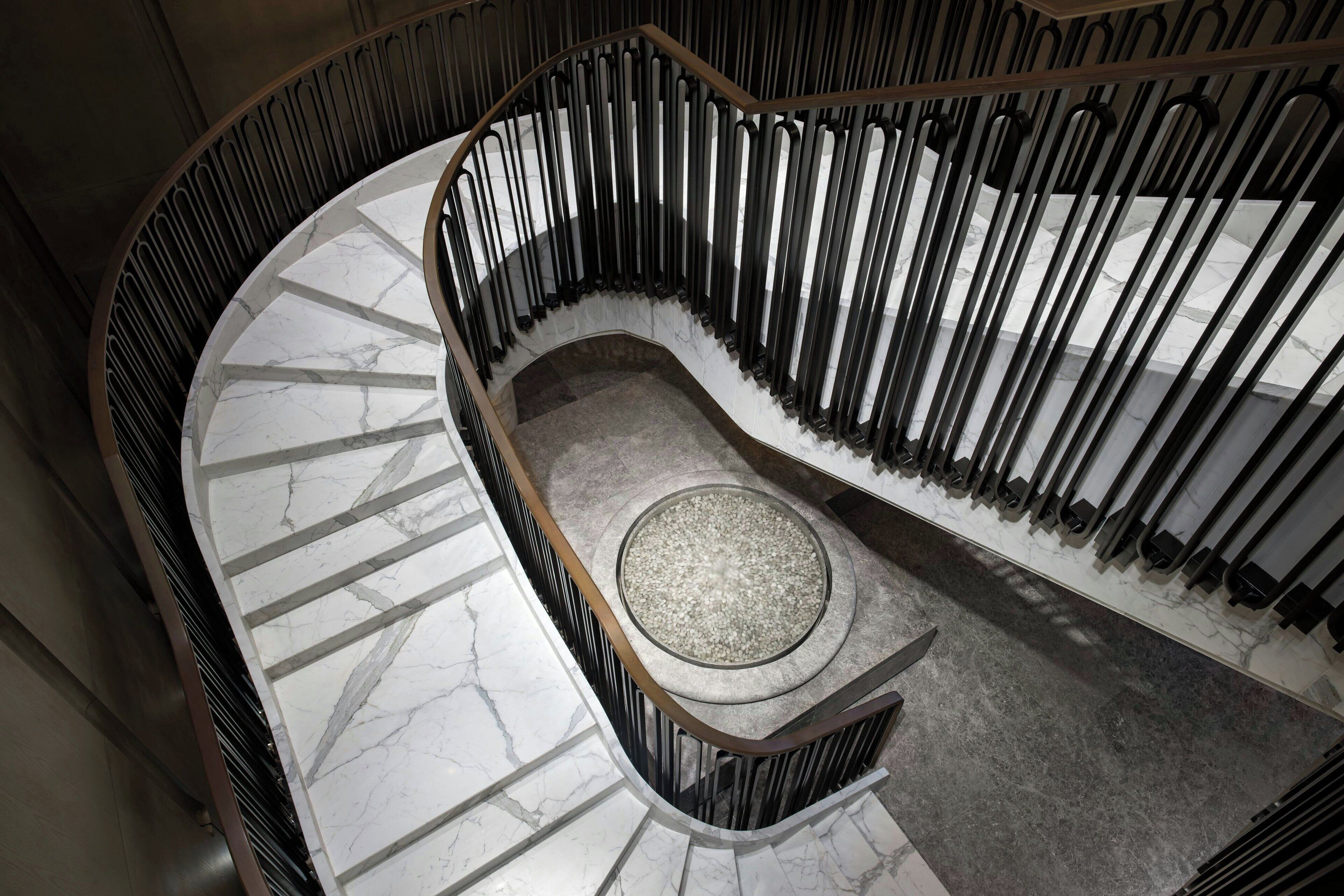 Uma escadaria em espiral com degraus de mármore e um patamar circular central.
