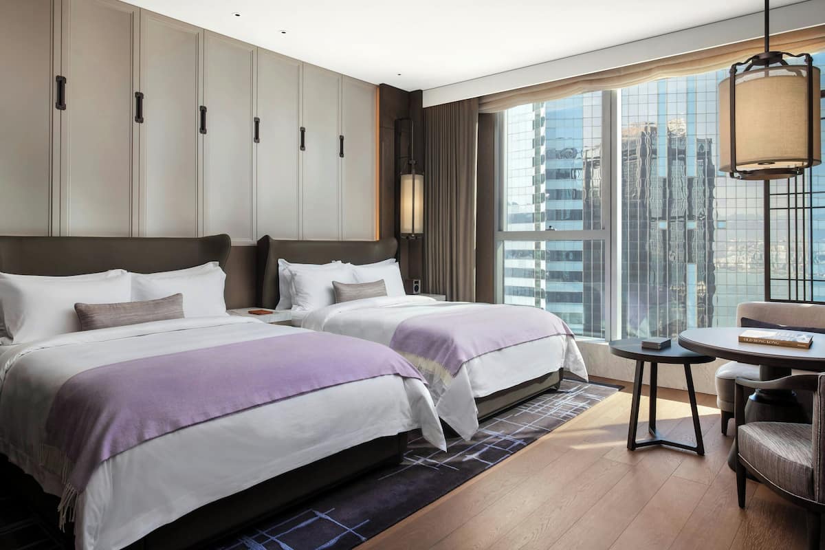 A hotel room with two beds, a small table, and a view of the cityscape.