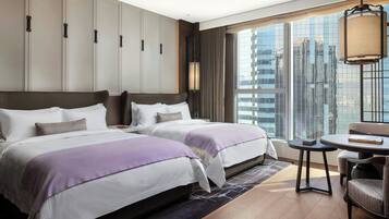 A hotel room with two beds, a small table, and a view of the cityscape.