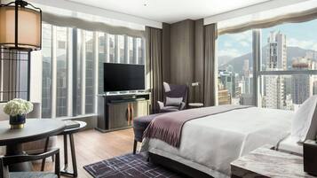 Quarto de hotel moderno com uma cama grande, uma escrivaninha com televisão, uma cadeira e vista para a cidade.