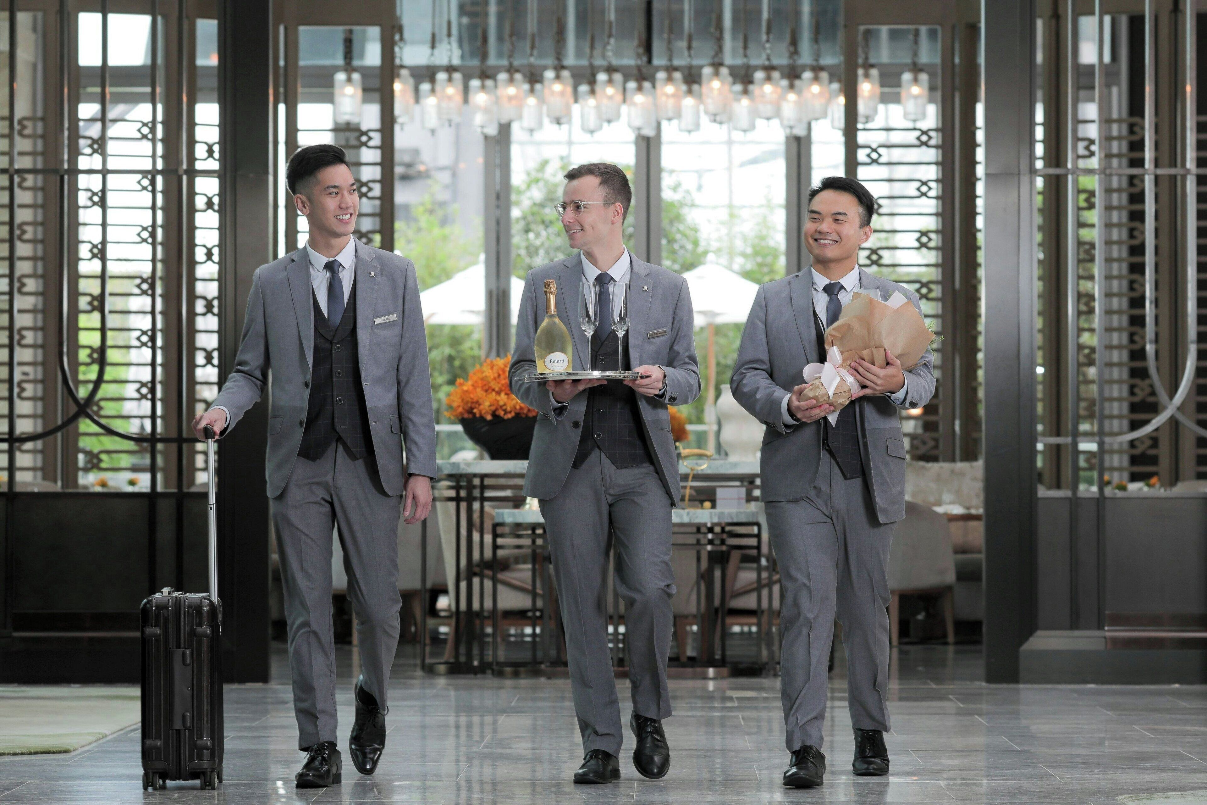 Three men in suits walking through a modern lobby with a dining area in the background.