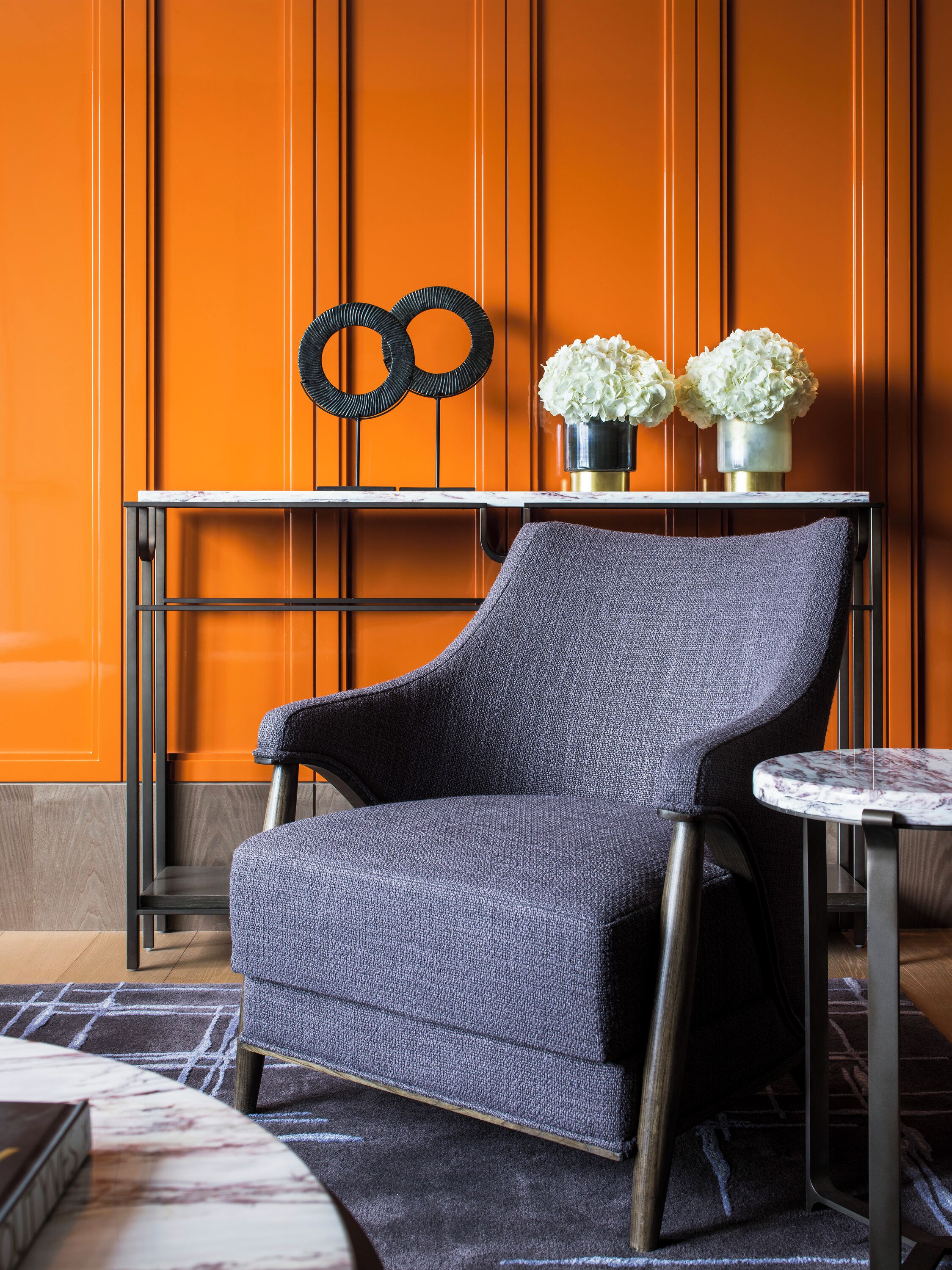 A modern room with an orange wall, a grey armchair, a small round table, and a metal-framed side table.