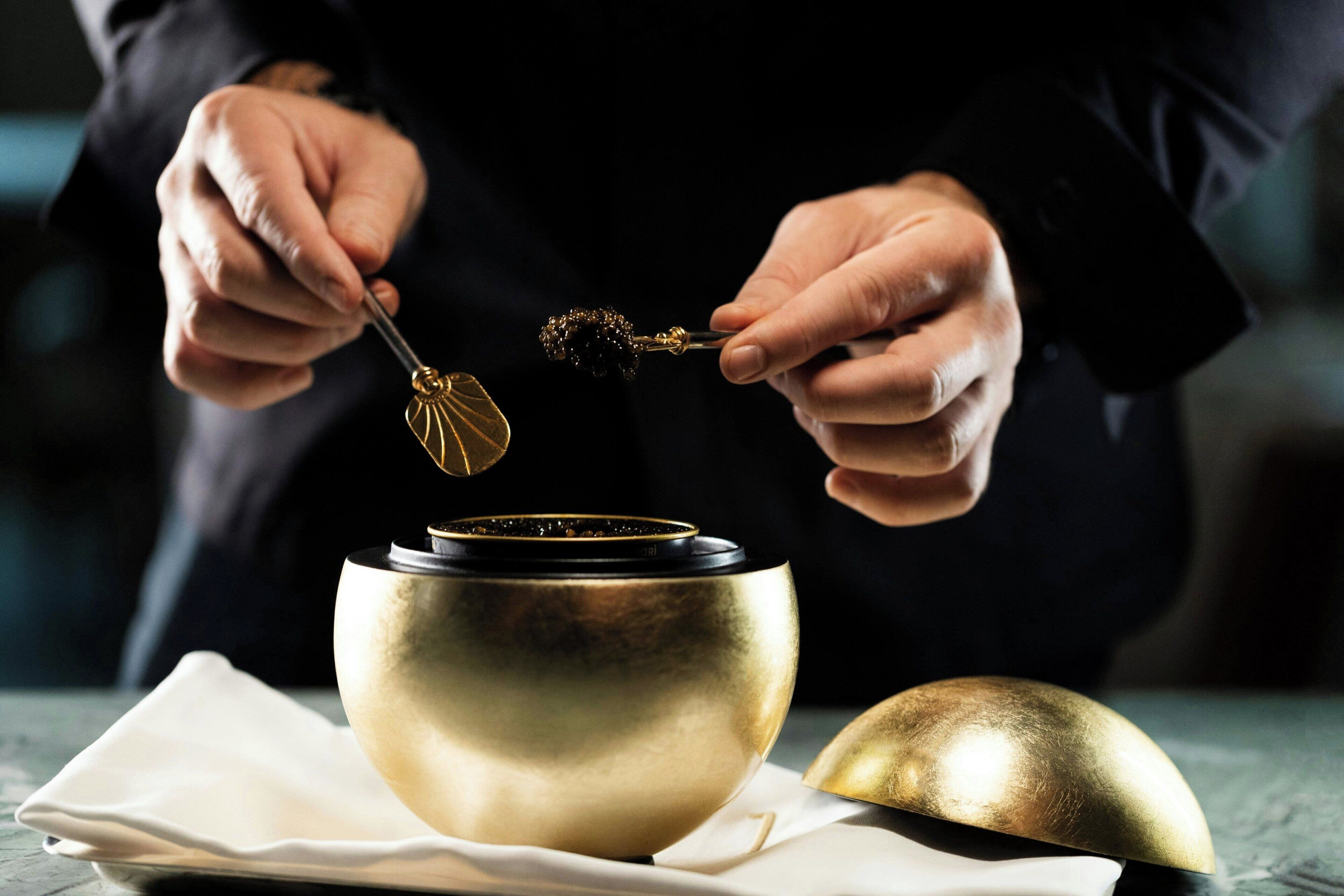 A person holding a spoon over a golden bowl, with a napkin and another bowl on the table.