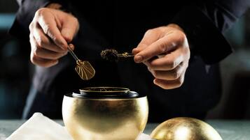 A person holding a spoon over a golden bowl, with a napkin and another bowl on the table.