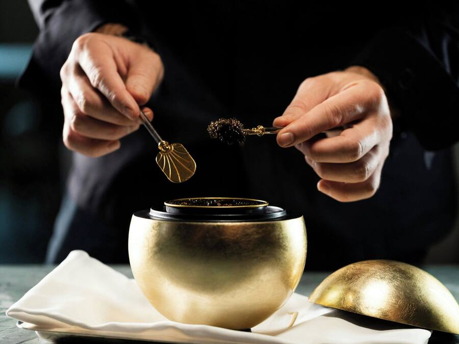 A person holding a spoon over a golden bowl, with a napkin and another bowl on the table.