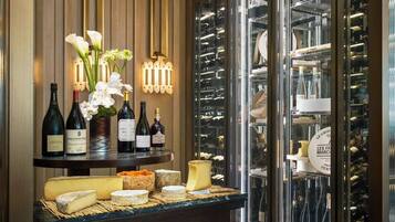 A wine cellar with a selection of bottles and cheeses on a table, surrounded by wooden paneling and glass display cases.
