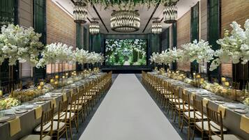 A long banquet hall with a central aisle, tables set with white tablecloths and candles, and a large screen at the end displaying a garden scene.