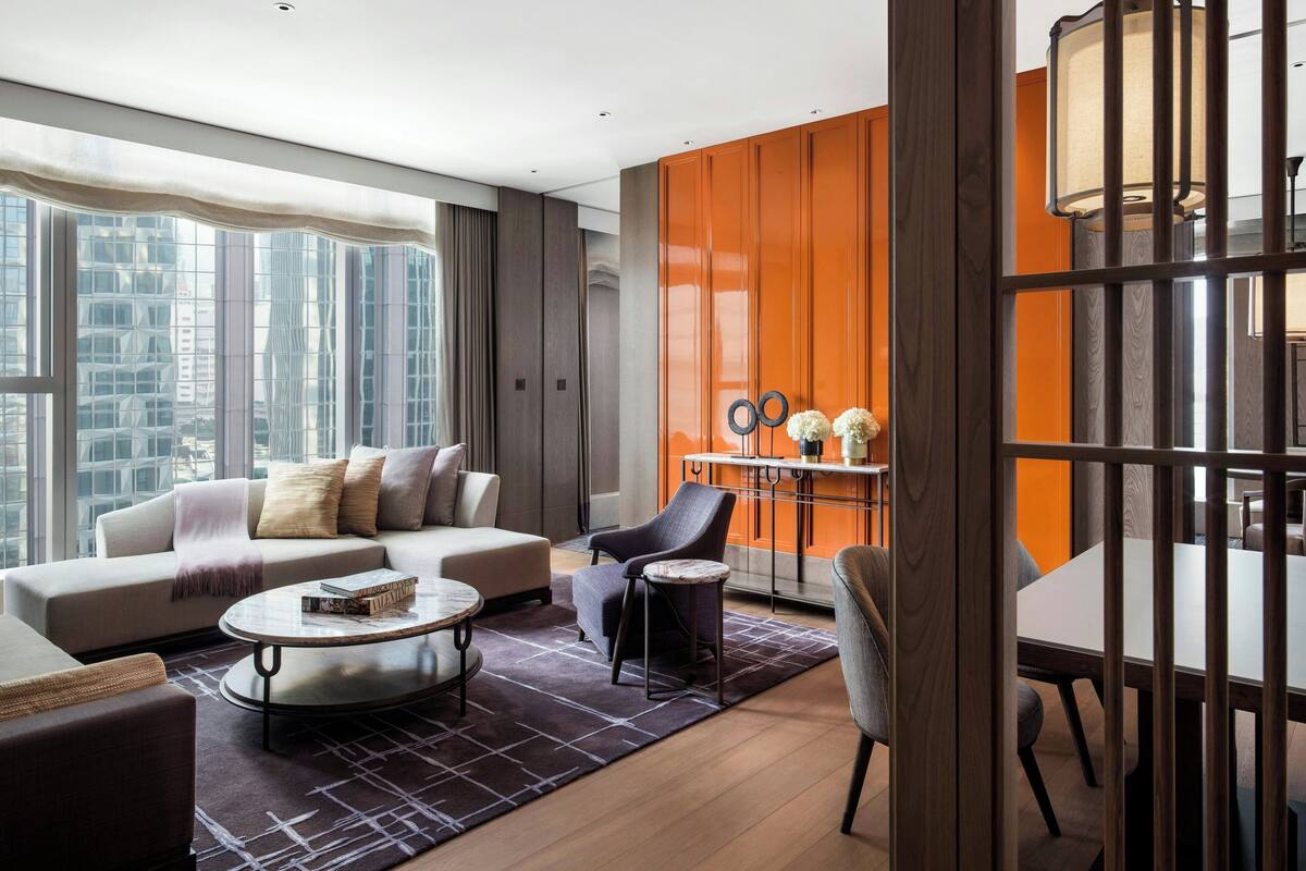 A modern living room with a sofa, armchairs, a coffee table, and a dining area with a table and chairs.