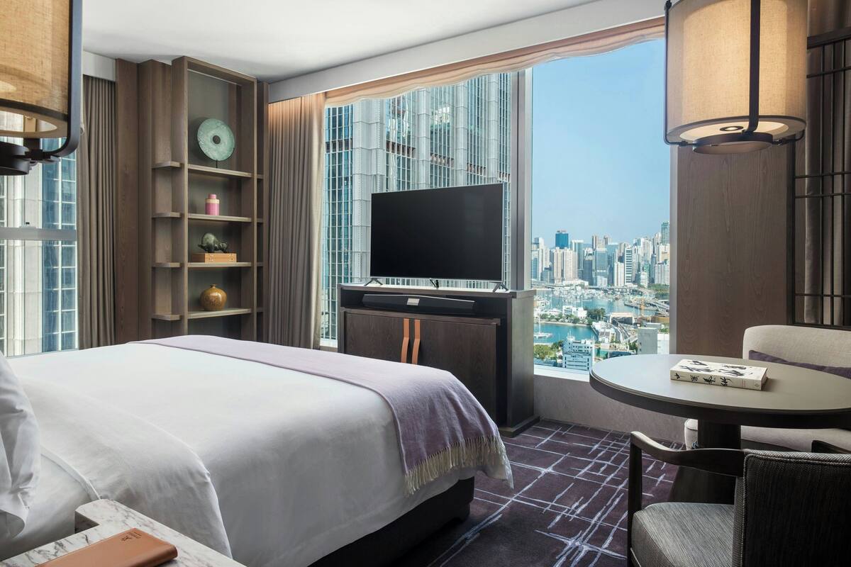 A hotel room with a bed, a TV, a small table, and a city view.