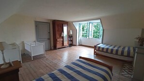 Ett rum med två sängar, ett vitt skrivbord, en dörr och ett fönster med utsikt över grönområden.