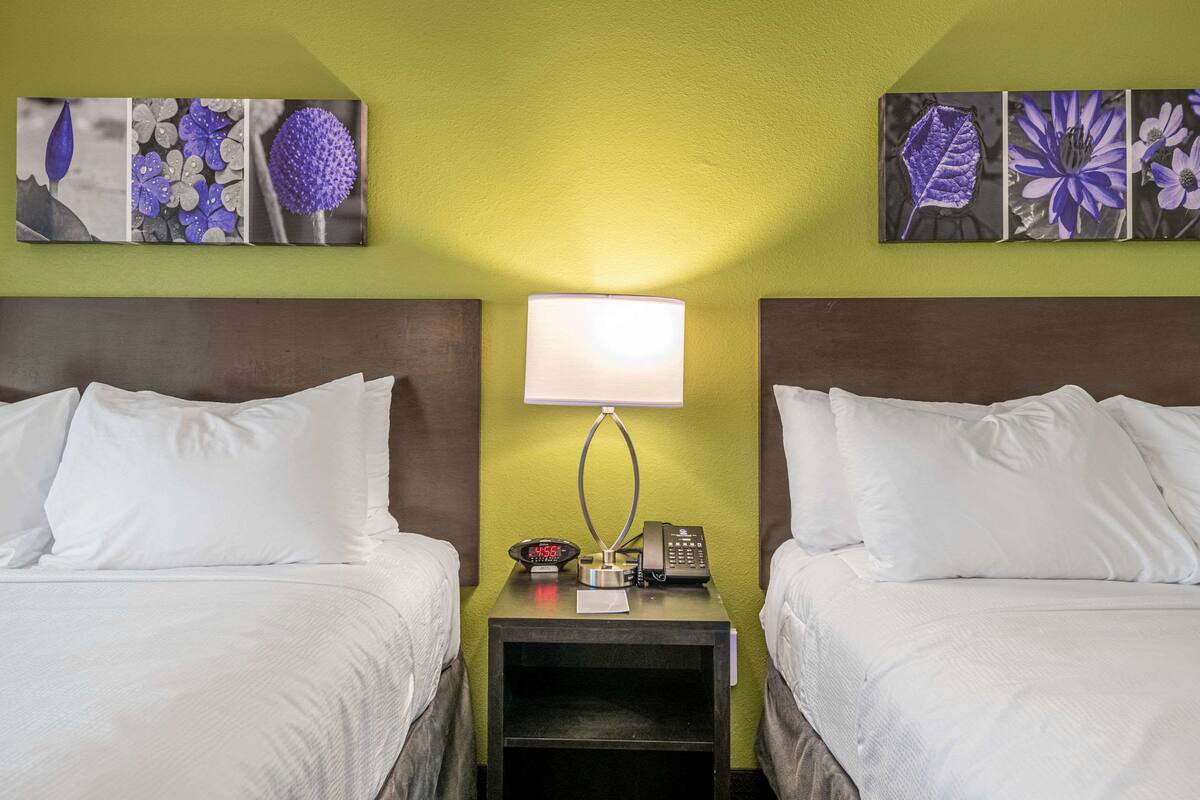 Ein Hotelzimmer mit zwei Betten, einem Nachttisch mit Lampe, einer Uhr und einem Telefon.