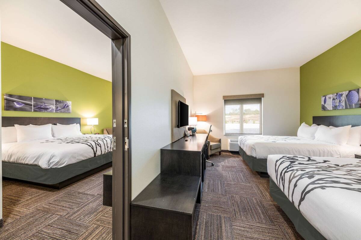 Ein Hotelzimmer mit zwei Betten, einem Schreibtisch, einem Flachbildfernseher und Bildern an den Wänden.